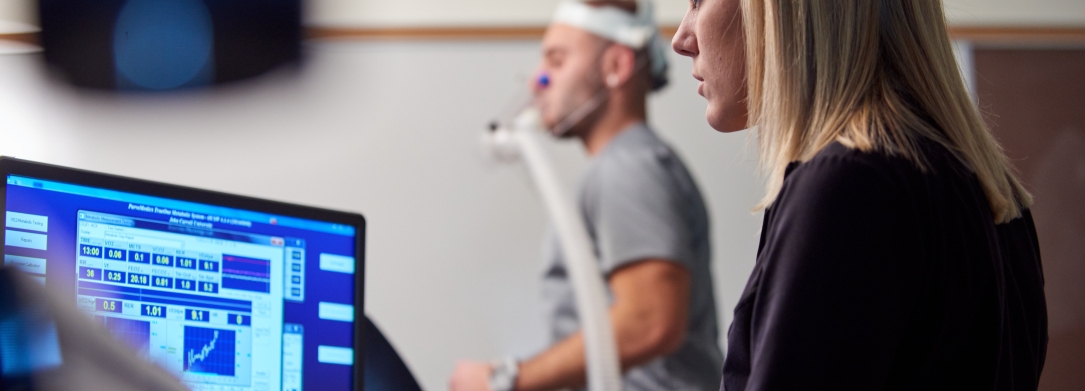 Young female teacher looking at a screen measuring a man's heart rate as he runs on a treadmill